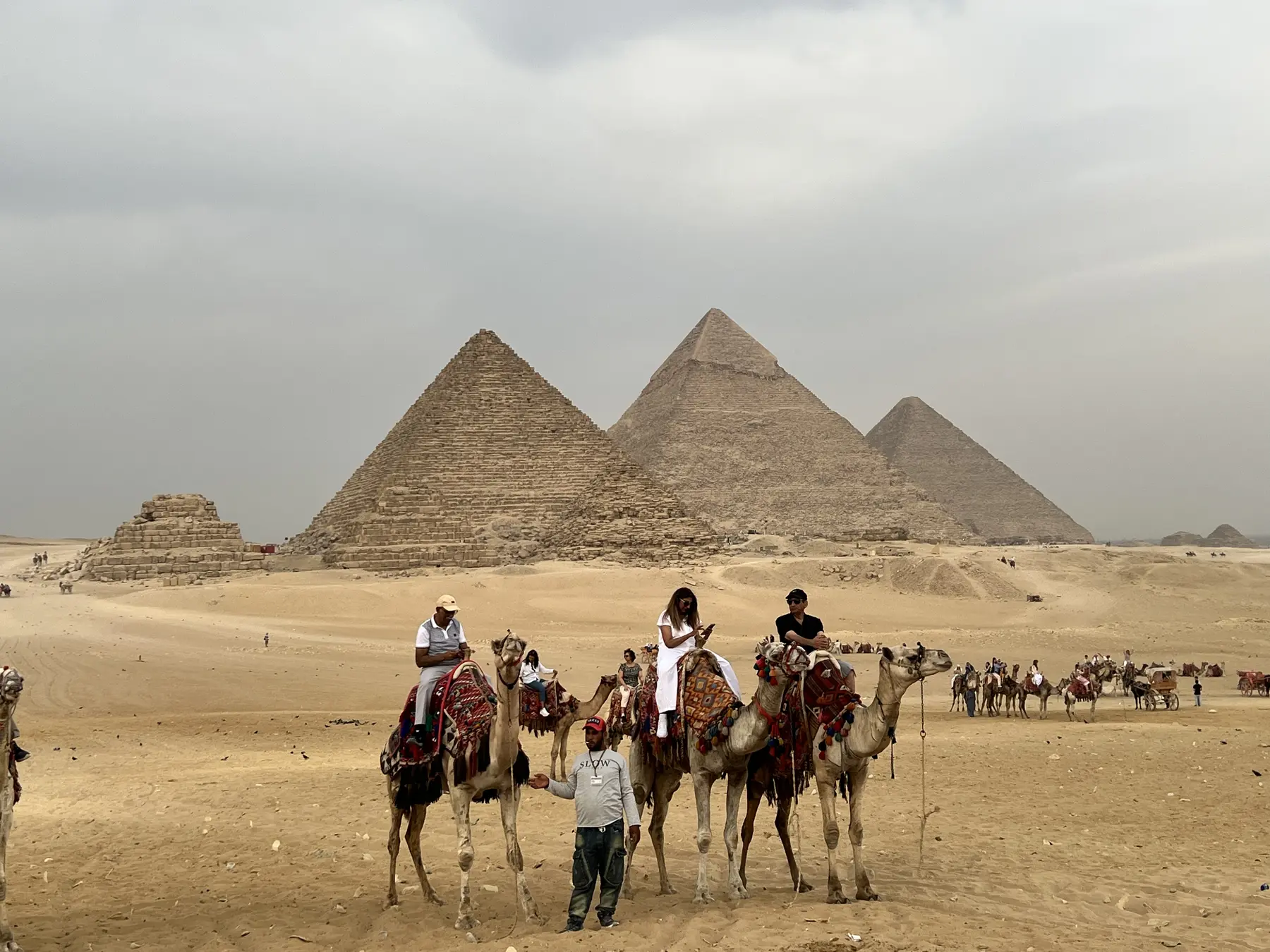 Atenara travellers riding camels with the Giza pyramids behind them